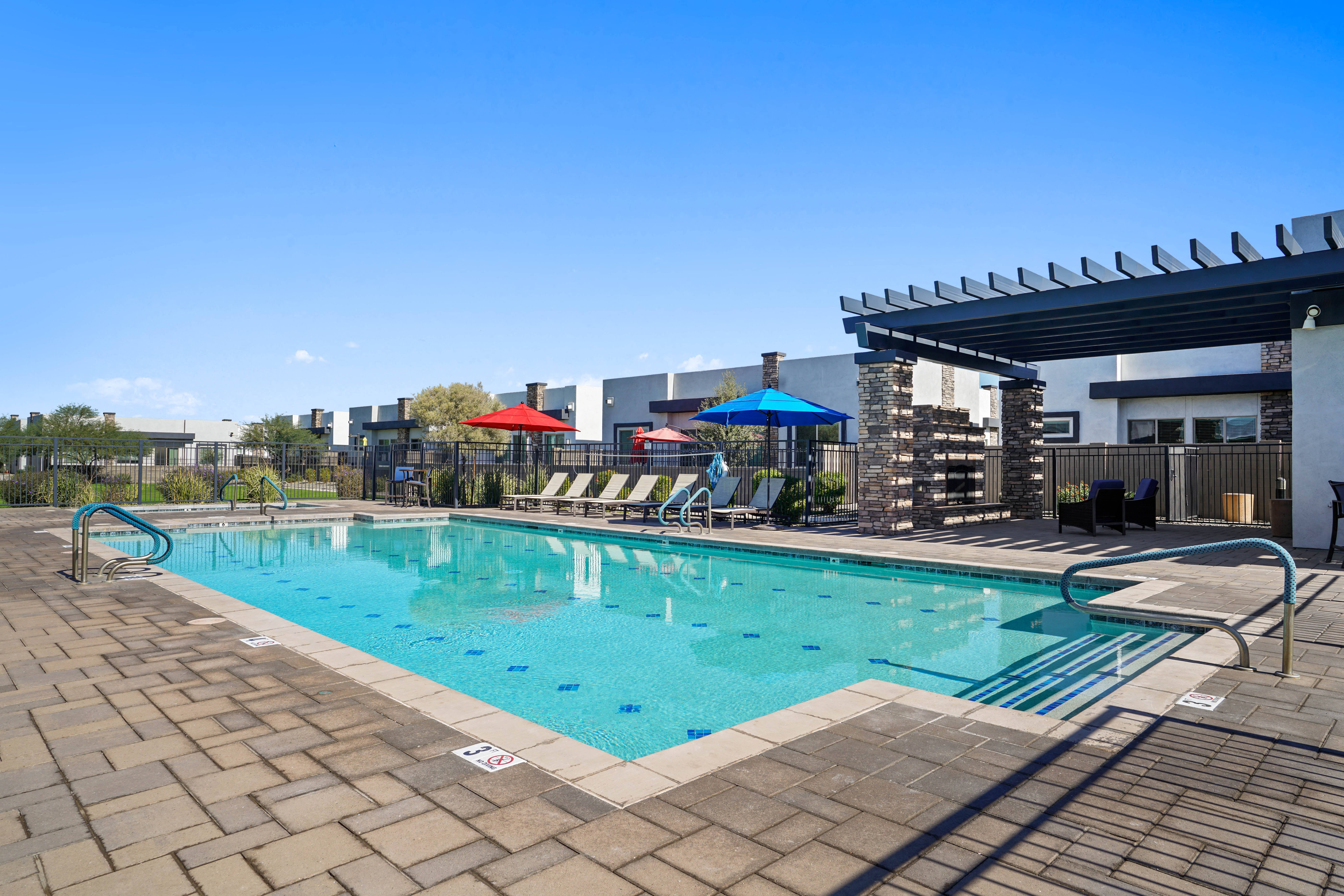 a resort style pool with lounge chairs and umbrellas next to a building at Olive Queen Creek Apartments, Queen Creek, AZ, 85142